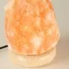Glowing peach-orange Himalayan salt lamp resting on a speckled stone base.