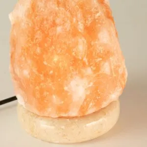 Glowing peach-orange Himalayan salt lamp resting on a speckled stone base.