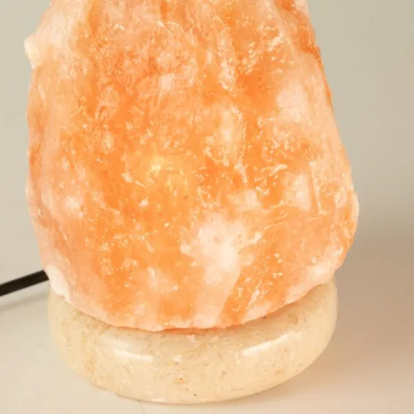 Glowing peach-orange Himalayan salt lamp resting on a speckled stone base.