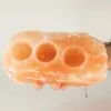 Hands holding a natural pink Himalayan rock salt tealight candle holder with three indents.