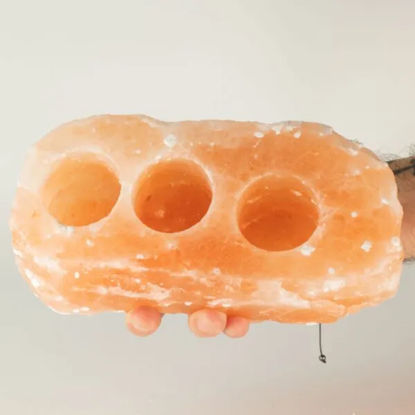 Hands holding a natural pink Himalayan rock salt tealight candle holder with three indents.