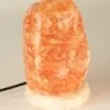 An unlit, rough-textured Himalayan pink salt lamp on a round speckled stone base.