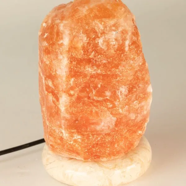 An unlit, rough-textured Himalayan pink salt lamp on a round speckled stone base.