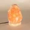 Glowing pink Himalayan salt rock lamp set on a cream stone base.