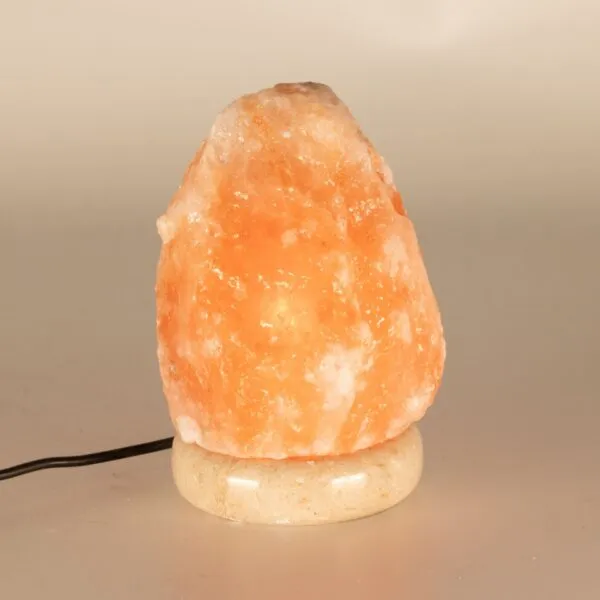 Glowing pink Himalayan salt rock lamp set on a cream stone base.