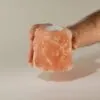 Tealight Candle Holder Himalayan Salt Pink Rough Cut A hand holding a rough-cut pink Himalayan salt tealight candle holder.