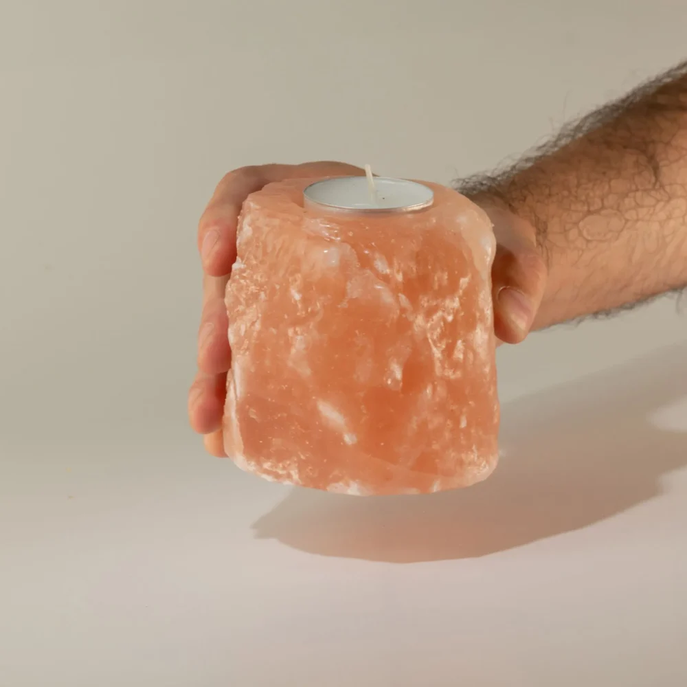 A hand holding a rough-cut pink Himalayan salt tealight candle holder.