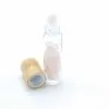 Rollerball Bottle, Glass Bamboo, Pink Rose Quartz Chips Clear glass rollerball bottle filled with pink rose quartz chips beside a bamboo cap.