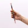 Hand holding a pink rose quartz chakra crystal wand with rainbow gemstones.