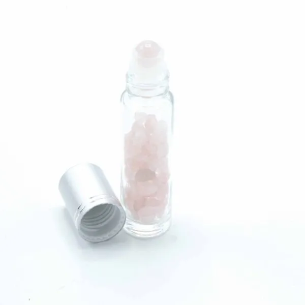 Rose quartz rollerball bottle filled with pink gemstone chips next to a brushed aluminium cap.