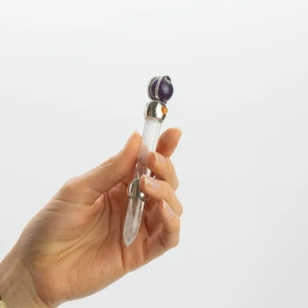 A hand holding an amethyst and carnelian crystal massage wand with dual gemstone tips.