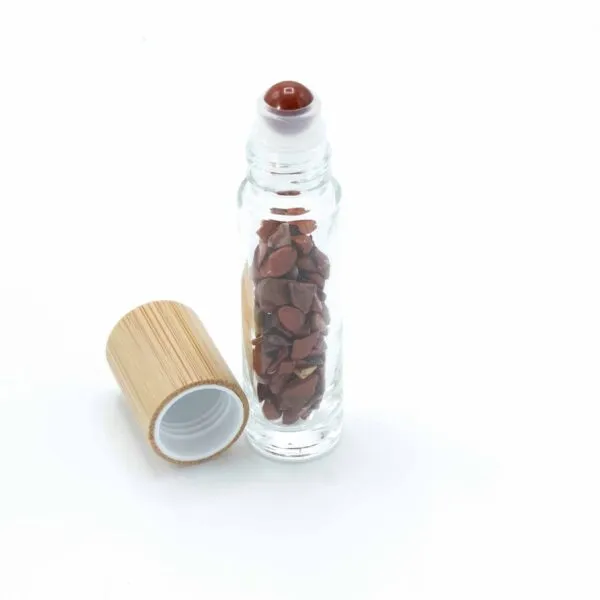 Glass roller bottle filled with red jasper crystal chips beside a bamboo cap.