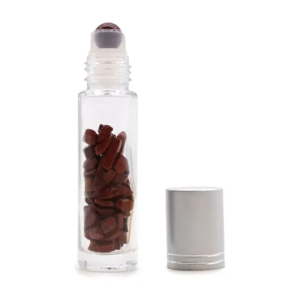 Clear glass roller bottle filled with Red Jasper gemstones beside a brushed metal cap.