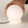 USB Ball Salt Lamp Himalayan Stone Base White Soft Glow A hand lifting a glowing white USB Himalayan salt lamp from its stone base.