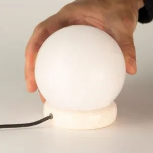 A hand lifting a glowing white USB Himalayan salt lamp from its stone base.
