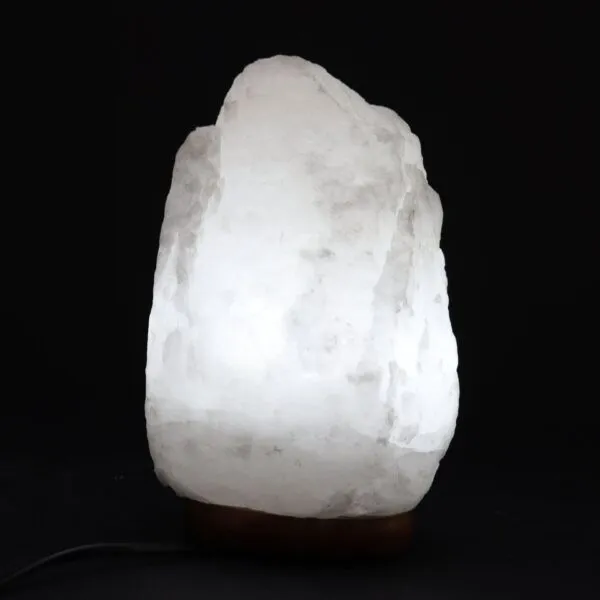 Illuminated natural white rock salt lamp glowing on a dark wooden base.