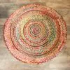 Multicoloured round braided jute rug featuring a spiral pattern on a distressed wood floor.