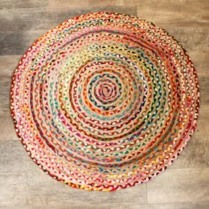 Multicoloured round braided jute rug featuring a spiral pattern on a distressed wood floor.