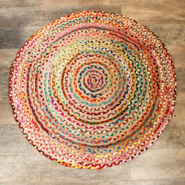 Multicoloured round braided jute rug featuring a spiral pattern on a distressed wood floor.
