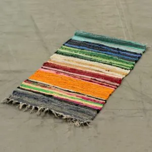 Multicoloured woven cotton rag rug with cream fringe trim on a concrete floor.