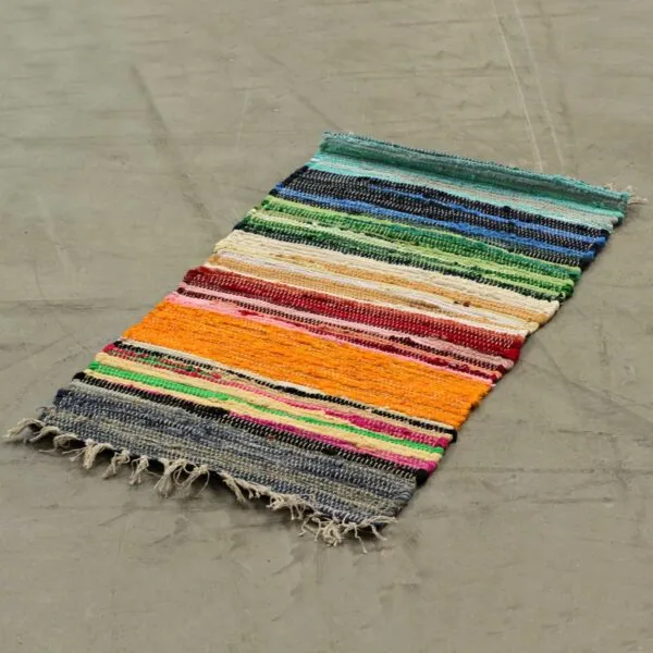 Multicoloured woven cotton rag rug with cream fringe trim on a concrete floor.