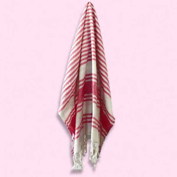 Red and white striped Turkish cotton peshtemal towel with fringes hanging from a hook.