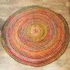 Round red braided yarn rug with a multicoloured spiral pattern on light wood floorboards.